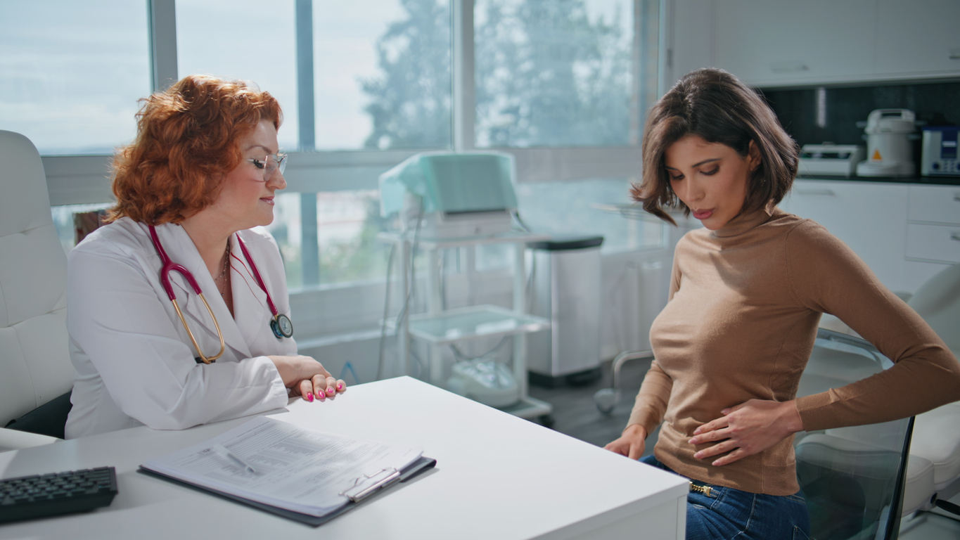 Clinic patient feeling stomach discomfort talking with woman physician closeup